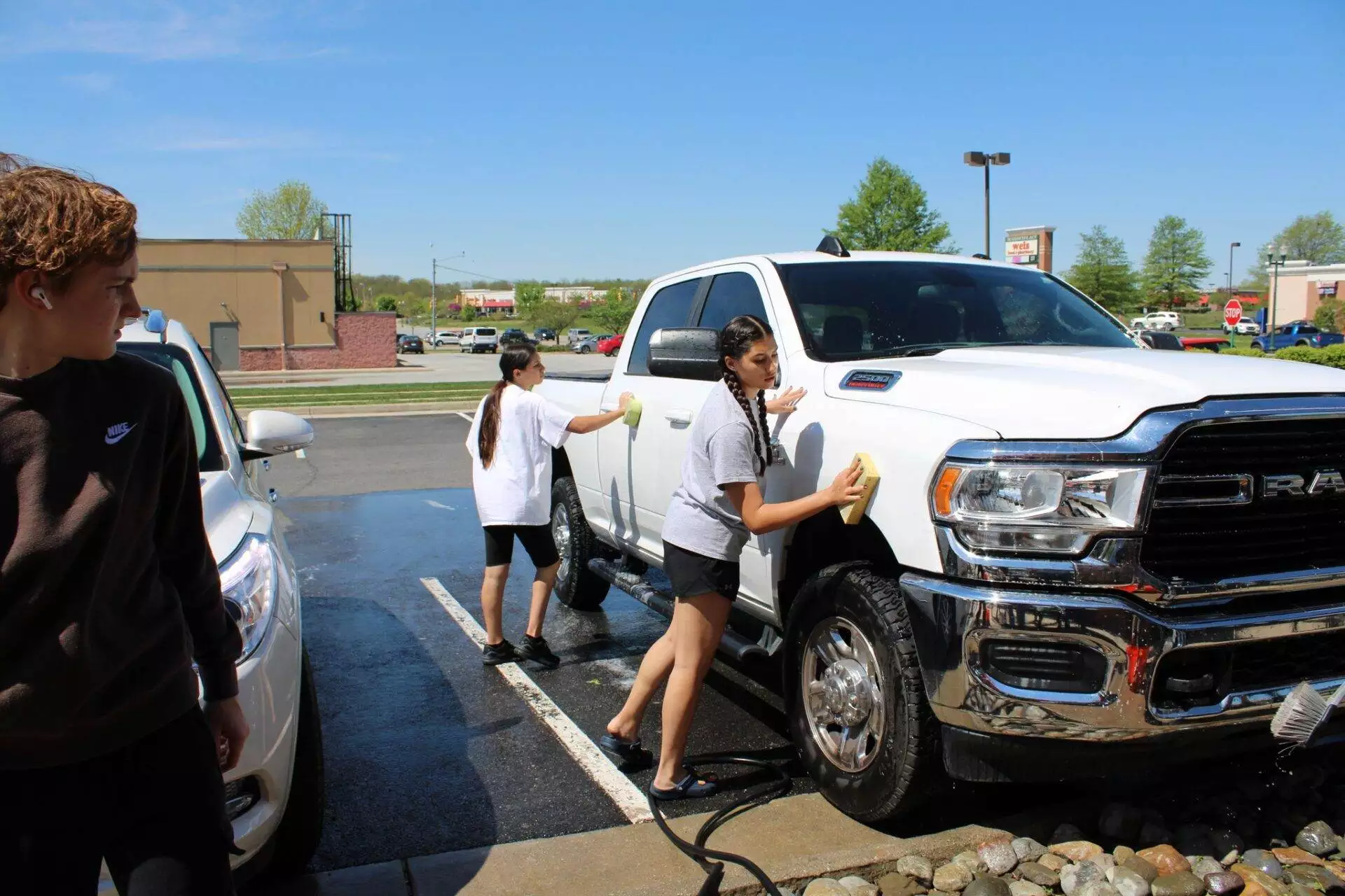 Three people washing a white pickup truck in a sunny parking lot.