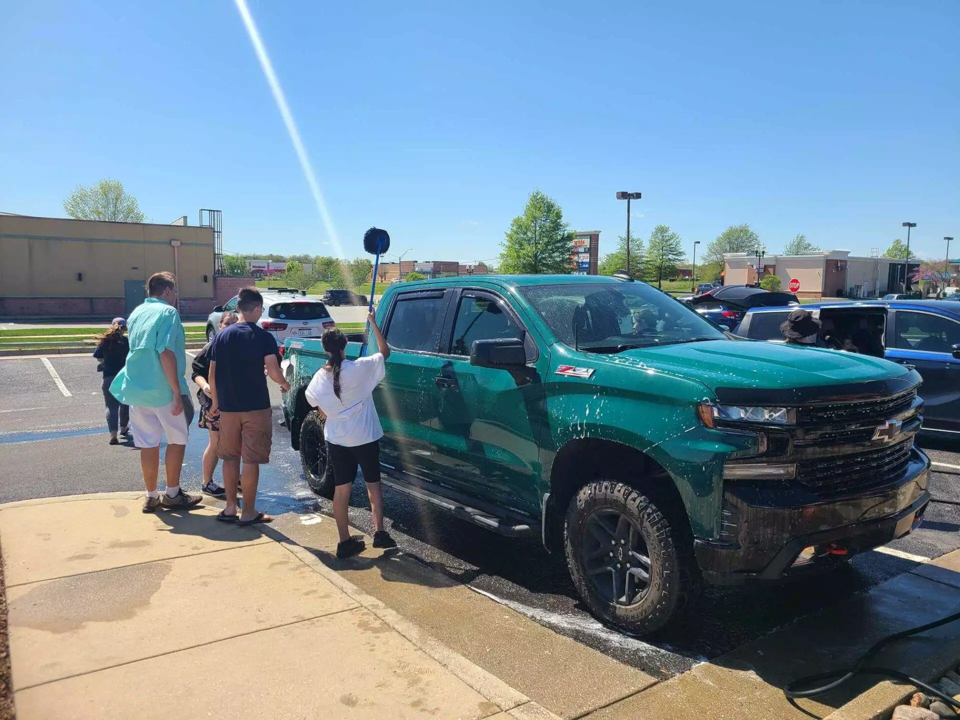 A group of people washing a green chevrolet truck at a community car wash event on a sunny day.